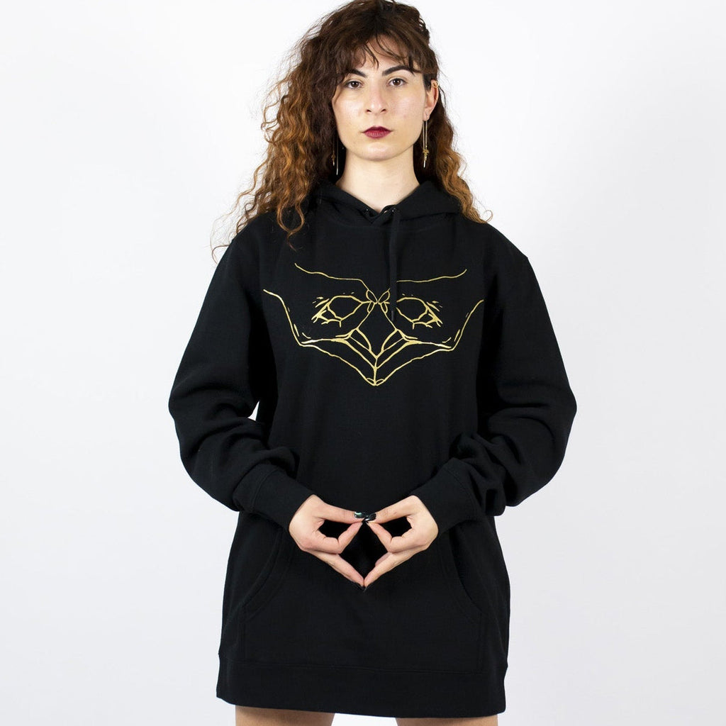 Person wearing a black hoodie with a gold wombpower hand design 