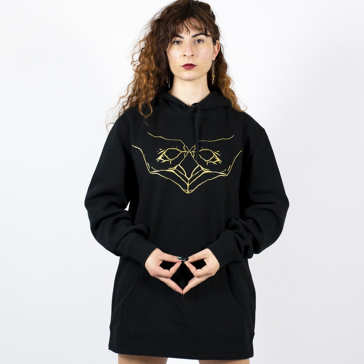 Person wearing a black hoodie with a gold wombpower hand design 